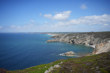 An expansive view of the green, rolling headlands of the Brittany coast under a sky with scattered clouds.