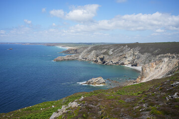 Fototapeta premium A vast coastal landscape in Brittany, showing rolling hills covered in green grass and purple heather meeting the sea.