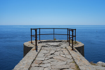 A weathered stone pier or viewpoint provides a stunning lookout over the calm blue sea on the coast of Brittany.