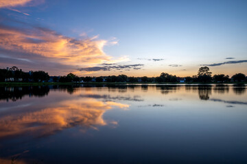 Golden Hour Sky Reflected on a Calm Lake at Sunset. A breathtaking view of a golden sunset over a calm lake with dramatic clouds reflecting on the still water. 