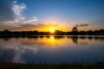 Sunset Over the Lake with Golden Reflections and Silhouetted Trees. The sun sets over a peaceful lake, casting golden reflections on the water’s surface. 