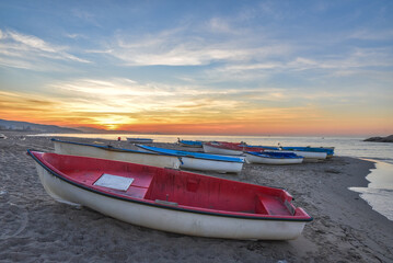 Fototapeta premium small wooden Fishing row boat on sandy beach in Mediterranean sea, White fishing boats by the sea, Boat on the beach at sunset time, A Small Boat Moored on a Beach. coastline, In Jijel Algeria Africa.