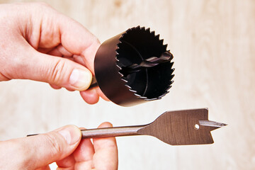 Spade bit and hole saw drill bit for woodworking held in hands close to each other ready to be...