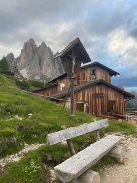 Citt&agrave; di Carpi Mountain Hut in the Dolomites &ndash; Peaceful Evening Scene with Wooden Bench and Cross Overlooking a Bucolic Alpine Landscape, Soft Light and Tranquil Atmosphere in the Italian Alps