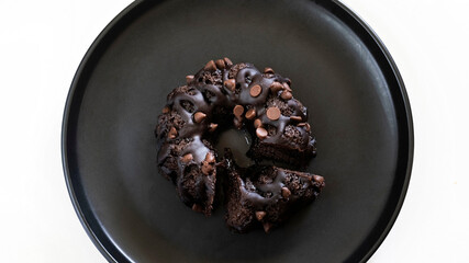 Top view of a chocolate cake with a slice cut off on the side, on a black plate.