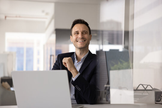 Middle-aged Hispanic businessman smiling, feeling satisfied with career, get good news about promotion or career growth, working in office seated at desk with laptop using new, innovative technologies