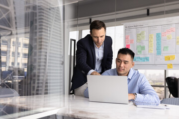 Mentor helps with online task completion to Asian male apprentice during meeting or briefing in...