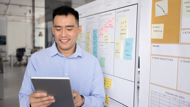 Focused Asian professional man sharing links or resources to colleague related to topic or joint task, corresponds to corporate client, provide consultation or assistance remotely using digital tablet