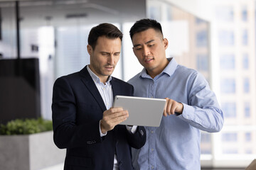 Collaboration, problem-solving during teamwork. Two diverse professional men working together in office using tablet, discuss joint task completion, reviewing information, learn new corporate software