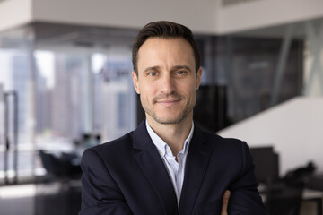 Head shot close up portrait of professional man dressed in formal jacket posing in city office, stare at camera with confident and contented expression. Career growth, human resources, achievements