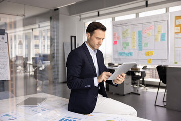 Fototapeta premium Man takes notes on digital documents, accessing project management software to track progress, search information, preparing slide show or presentation on tablet for upcoming meeting with shareholders