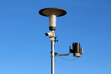 A modern weather station pole features environmental sensors, surveillance camera, and rain gauge,...