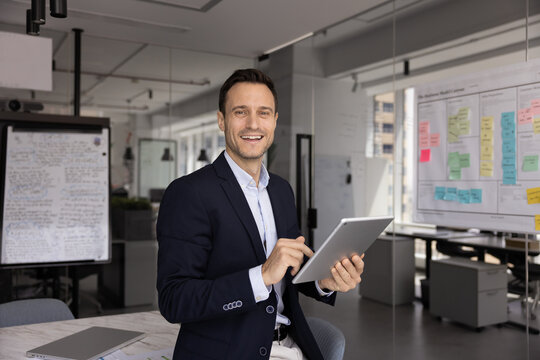 Office portrait of smiling middle-aged businessman, project manager or analyst in suit looking at camera, holding digital tablet, enjoy online workflow, using new AI, innovative business technologies