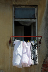 Light floral and monochrome dresses hang on a line outside a weathered, old plastered building with...