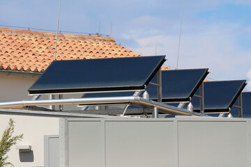 Three large solar water heating collectors are mounted on a building rooftop, with an interconnected stainless steel pipe system for distributing renewable thermal energy