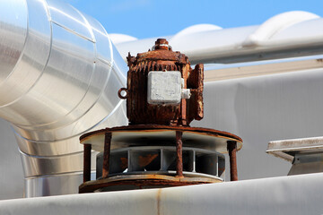 A heavily corroded rooftop exhaust fan motor exhibits extensive rust and weather damage,...