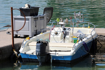 A compact blue and white motorboat is secured at a concrete pier, featuring an outboard engine,...
