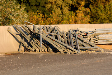 Large metal road safety barriers are stacked and leaning against a concrete wall, waiting for...