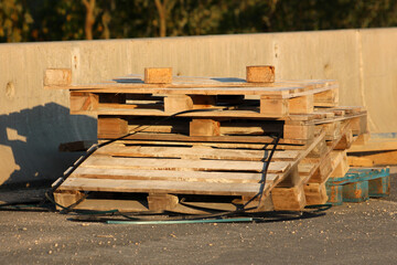 Multiple old wooden pallets are stacked haphazardly on asphalt, showing surface wear and some...