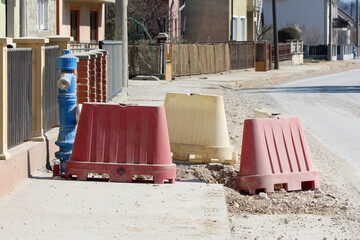 Plastic red and yellow barricades mark a sidewalk under repair beside a blue fire hydrant, showing...