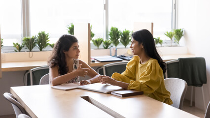 Two serious professional women, colleagues, client and manager lead talk sit at desk with laptop in modern office, share ideas, selling company services, looking interested while working on joint task