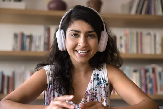 Webcam view Indian woman wear wireless headphones look at camera leading digital talk with colleague or client, share information, teaching learner via videocall. Blogging, social media icon portrait