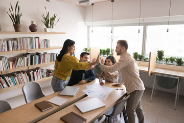 Obraz premium Happy businesspeople, staff members team giving high five gesture, gathered in modern boardroom, express support, showing unity, celebrate joint achievements, sales or career growth. Business success