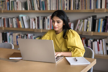 Young Indian woman employee or student working on laptop, studying online using website or internet resources, read e-mails, respond on business mails, preparing document or presentation for meeting