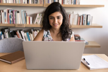 Woman immersed in work on project or studying using laptop in cozy workspace, notepad nearby for taking important notes, looks focused, engaged in task completion, attending online classes or webinar
