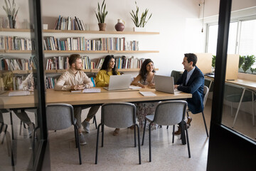 Group of multinational professionals take part in team meeting in modern office, sit at table with...