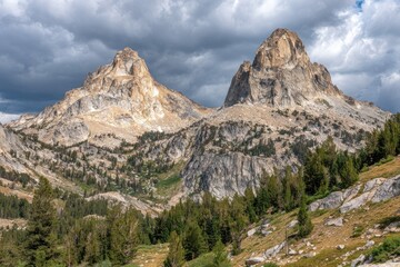 Two rocky mountain peaks rise above a valley filled with pine trees under a cloudy sky