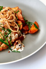 Deliciously Prepared Chicken Dish Topped with Crispy Onions and Accompanied by Crispy Potatoes and Fresh Herbs on a Elegant Gray Plate