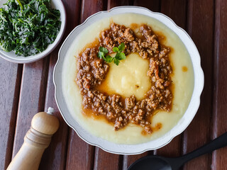 Polenta with bolognese sauce, typical Brazilian dish on a white plate with a wooden background