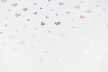 Multiple small iridescent heart shapes are isolated on a clean white background, creating a minimal...