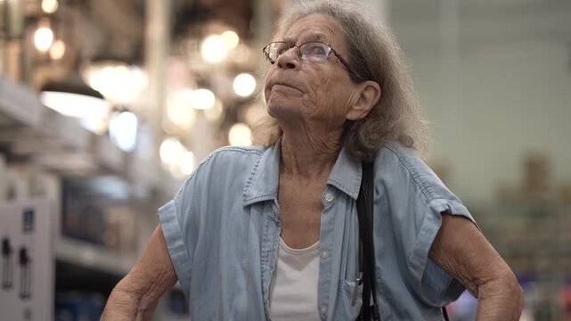 An elderly woman using a walker explores the aisles of a hardware store searching for home remodeling supplies to enhance her living space.