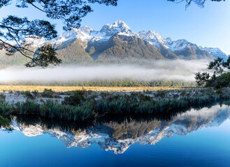 Mirror Lake, low lying fog and snow colored peaks on a clear winter day in Milford Sound, New Zealand