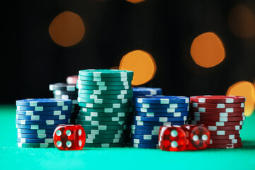 Casino chips and dice on green table against blurred lights, closeup