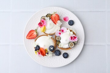 Delicious dessert. Tasty tartlets with cream, berries and flowers on white tiled table, top view