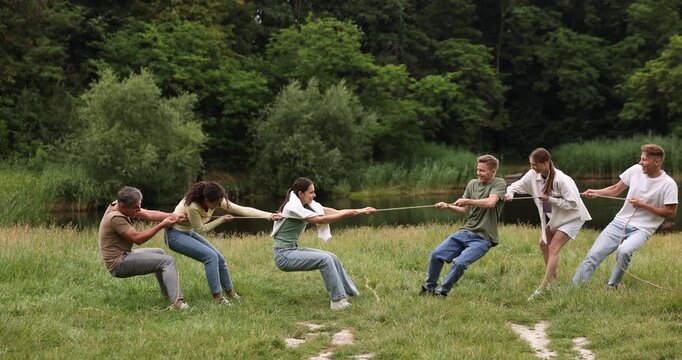 Team building. Group of happy people playing tug of war with rope outdoors