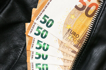 Fifty euro banknotes in black leather jacket. Hidden cash money in zipper pocket. Closeup view of...