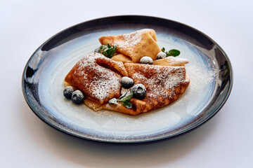 Delicious Crepes Topped with Blueberries and Powdered Sugar, Artfully Arranged on a Stylish Plate for a Gourmet Experience