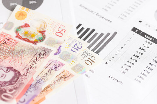 British pound banknotes on financial report. Money and data on white background. Economic growth statistics and currency concept. Business finance planning. Investment and revenue analytics tools.