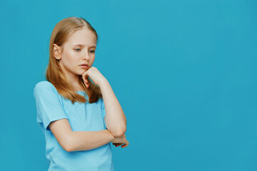 Thoughtful young girl in a blue t shirt posing against a turquoise background, conveying introspection and contemplation with her thoughtful expression