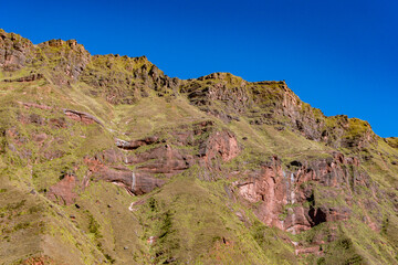 Detailed view of a rugged Andean rock formation, highlighting layers, colors, and resilient plant life