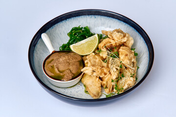 A vibrant dish showcasing crispy fried fish accompanied by a rich sauce, fresh lime, and complementary seaweed for a delightful culinary experience.
