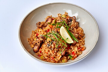 A Tasty Bowl of Fried Rice with Octopus, Fresh Vegetables, and a Splash of Lime Garnish for a Refreshing and Flavorful Meal Experience
