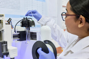 Female researcher with glove loads filament from spool into plastic 3D printer injector in laboratory