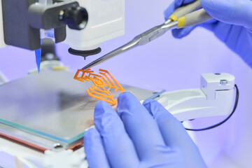 Scientist carefully separates a thin printed membrane from a 3D printer using tweezers in a clean...