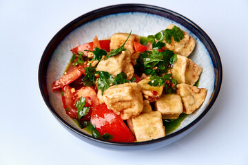 A vibrant dish featuring crispy tofu cubes mingled with ripe tomatoes, fresh herbs, and spices, creating a delightful vegetarian plate full of flavor.