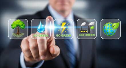 A businessman touches a digital screen displaying "go green" text and various environmental icons, including a tree, water drop, lightning bolt, factory with smoke, and a globe with a leaf.